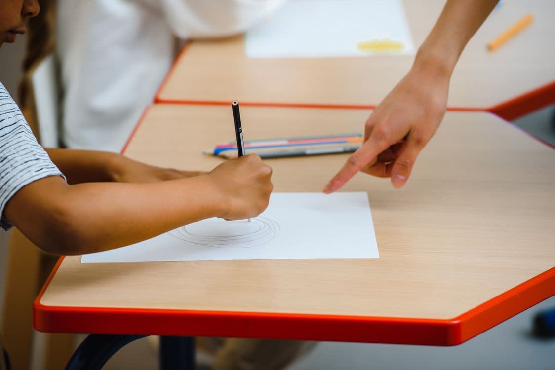 Un enfant dessine, guidé par le geste d’un adulte à ses côtés